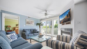 A living room with a sofa, armchair, glass coffee table, and a television mounted on the wall.
