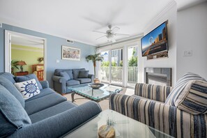 Ein Wohnzimmer mit Sofa, Sessel, Glastisch und einem an der Wand befestigten Fernseher.