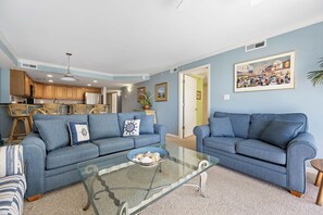 Ein Wohnzimmer mit zwei Sofas, einem Glastisch und einer Küche im Hintergrund.