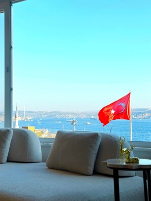 Ein Zimmer mit großem Fenster mit Blick auf ein Gewässer, eine Flagge und ein kleiner Tisch mit einem dekorativen Gegenstand.
