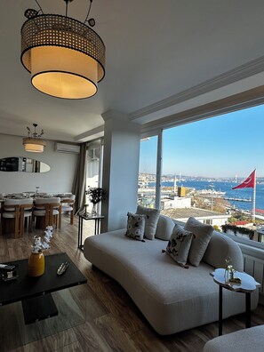 Ein modernes Wohnzimmer mit großem Fenster, Essbereich und Blick auf die Stadt.