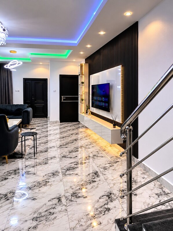 Ein modernes Wohnzimmer mit Marmorboden, einem an der Wand montierten Fernseher und einer Treppe mit Metallgeländern.