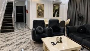 A modern living room with a marble floor, a chandelier, a staircase, and a dining area with chairs and a table. - Ileero Homes: The Manor | Executive 4-Bedroom (Lagos)