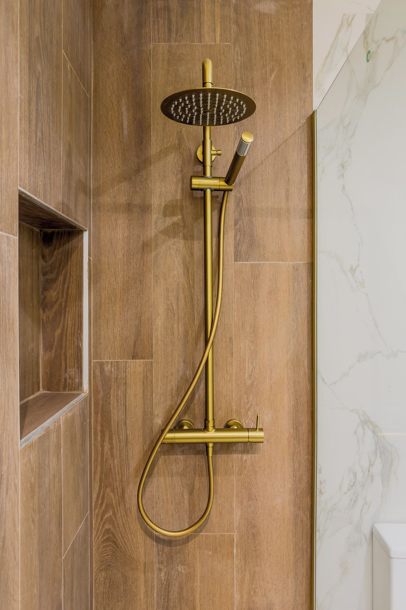 Eine an der Wand befestigte Duscharmatur mit goldfarbener Oberfläche, ein Handbrausekopf und ein flexibler Duschschlauch.