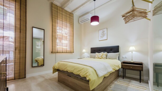 A bedroom with a bed, bedside tables, a mirror, and a hanging light fixture. - 2 bedroom apartment in Robador 39 (Barcelona)
