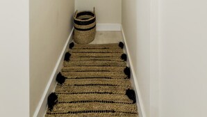 A narrow hallway with a wooden hanger rack, a basket, and a woven rug. - 2 bedroom apartment in Robador 39 (Barcelona)