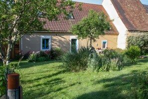 Une maison avec un toit en pente, un petit jardin agrémenté de diverses plantes et fleurs, et une clÎture en bois.