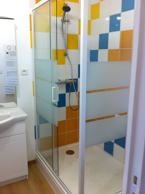 Une salle de bain moderne avec une douche à parois de verre, un lavabo blanc et un mur carrelé à motifs à carreaux.
