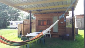 Un espace extérieur abrité comprenant un hamac, une table, des chaises et une structure en forme de cabane en bois.