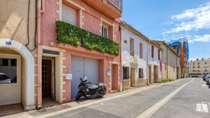 Une rue étroite bordée de bâtiments, un scooter garé et un ciel bleu dégagé.