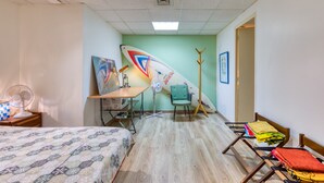 Une pièce comprenant un lit, un bureau, une chaise, une planche de surf et un porte-manteau.