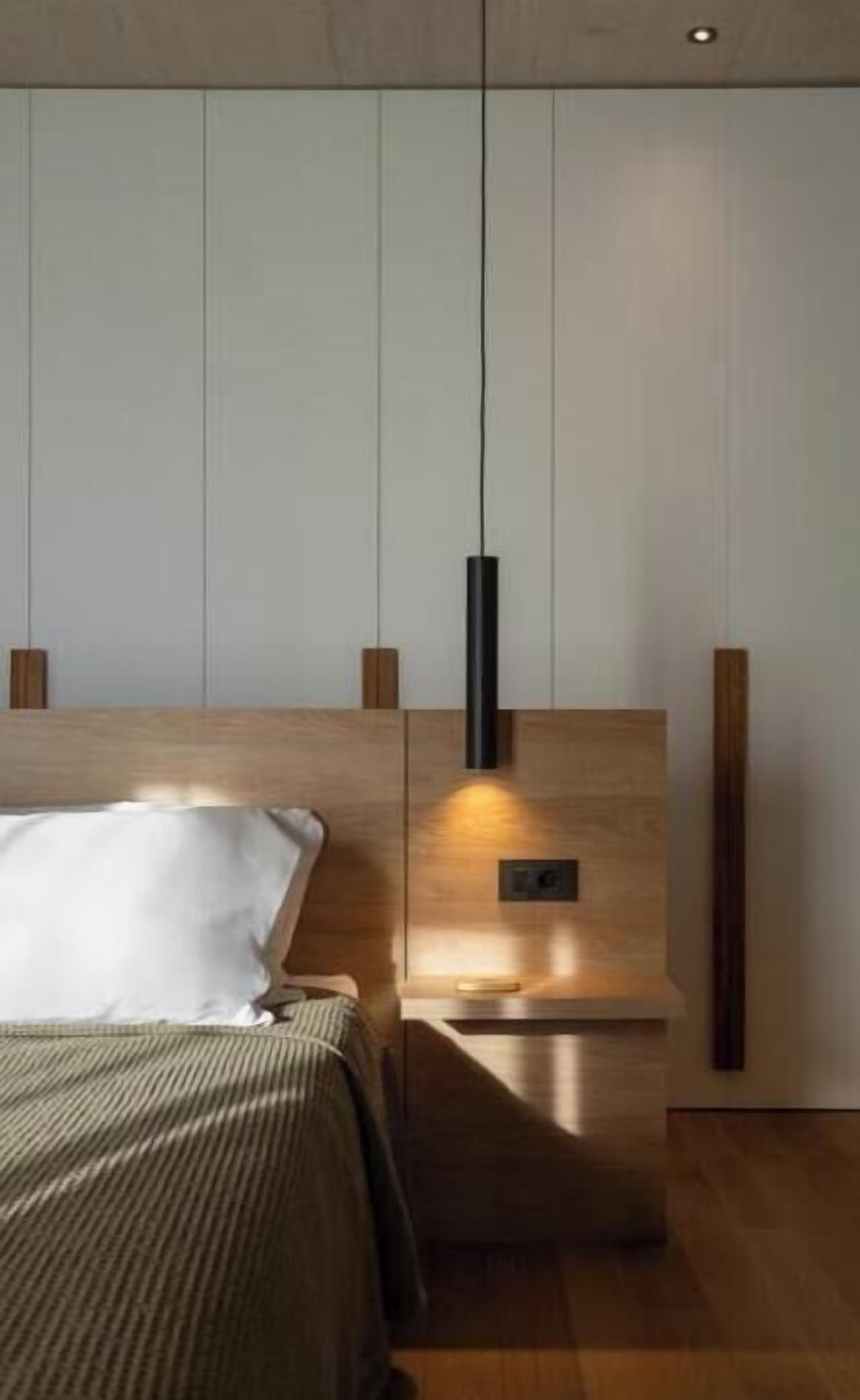 A modern bedroom with a wooden headboard, a bedside table, and a hanging pendant light.