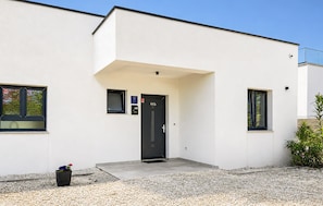 Ein modernes Gebäude mit einer schwarzen Tür, einem kleinen Eingang und einer Schotterauffahrt.
