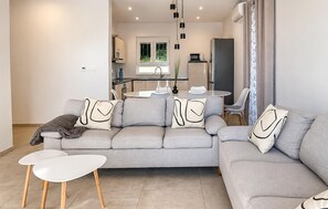 Ein modernes Wohnzimmer mit einem grauen Sofa, zwei weißen Beistelltischen und einem Essbereich mit einem runden Tisch und Stühlen.