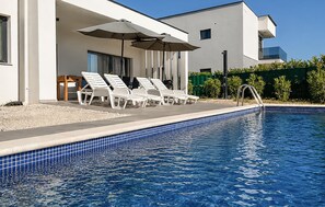 Ein Swimmingpool mit Liegestühlen und Sonnenschirmen, ein modernes Gebäude mit großen Fenstern und ein klarer Himmel.