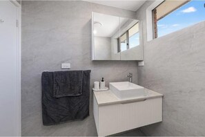 A modern bathroom with a white sink, a towel rack with a dark towel, and a large mirror. - affordable modern getaway with parks/cafe nearby (WOODPARK)