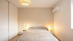A bedroom with a bed, two bedside lamps, a hanging light fixture, and an air conditioning unit. - Elegant 2-bedroom apartment-Near downtown (Périgueux)