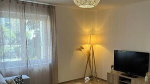 A modern living room with a sofa, a coffee table, a TV on a wooden stand, and a floor lamp. - Elegant 2-bedroom apartment-Near downtown (Périgueux)