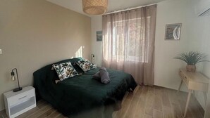 A bedroom with a bed, a bedside table, a hanging light fixture, a window with curtains, and a small plant on a side table. - Elegant 2-bedroom apartment-Near downtown (Périgueux)