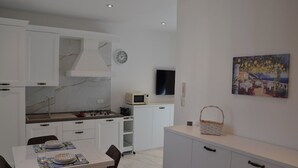 Une cuisine moderne avec des meubles blancs, une cuisinière à gaz, un four à micro-ondes et un coin repas avec une table dressée pour deux personnes.