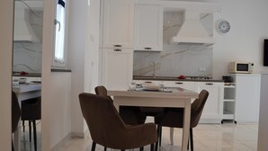 Une cuisine moderne avec des armoires blanches, une hotte en acier inoxydable, un four à micro-ondes et un coin repas comprenant une table et des chaises.