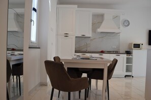 Una cucina moderna con mobili bianchi, una cappa aspirante in acciaio inossidabile, un forno a microonde e un'area pranzo con tavolo e sedie.