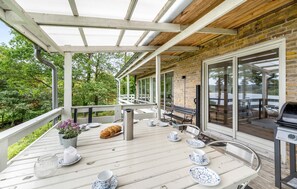 Une terrasse extérieure couverte, avec une table préparée pour le thé, un barbecue et une vue sur la verdure environnante.