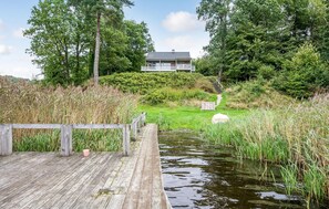 Une jetée en bois menant à une maison, avec une pelouse et un étang à proximité.