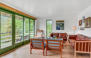 Une pièce spacieuse avec de grandes fenêtres, une table en bois, deux chaises, un canapé et un tableau accroché au mur.