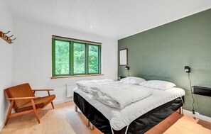 Une chambre à coucher avec un lit, une chaise, une fenêtre et une lampe fixée au mur.