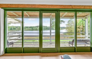 Une pièce dotée d’une grande porte-fenêtre coulissante qui donne sur une terrasse extérieure offrant une vue sur un lac et une forêt.