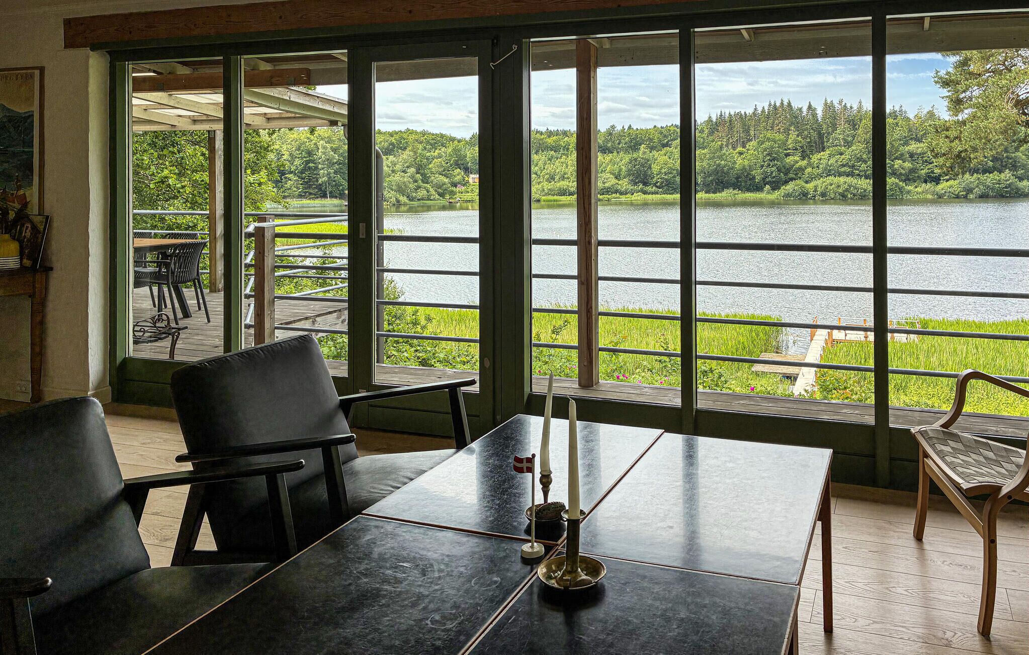 A room with a table and chairs, large windows with a view of a lake and forest.