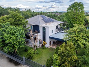 Et moderne hus i to etager med solpaneler, omgivet af frodig vegetation og en klar himmel.