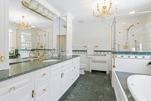 Une salle de bain luxueuse avec un grand miroir, un lustre, une baignoire et des toilettes.