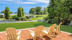 Pátio com cadeiras Adirondack e piso de tijolos, com vista para um lago e vegetação.