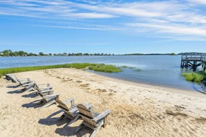 Ein Strand mit Holzstühlen und einem Steg, der ins ruhige Wasser führt.