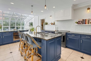 A modern kitchen with a large island, dark blue cabinets, and a glass-enclosed window.