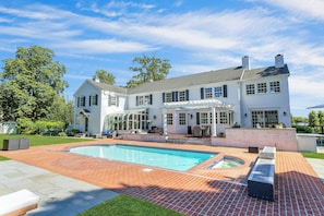 A large house with a swimming pool, a covered patio, and a well-maintained lawn.