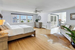 A bedroom with a wooden bed, a dresser, a mirror, a ceiling fan, and a view of the outside.