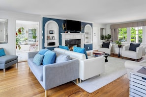 A modern living room with a fireplace, white sofas, and a large TV.