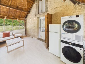 Ein Waschbereich mit Waschmaschine und Trockner, einer hölzernen Bank, einer Couch und Blick ins Freie durch große Fenster.