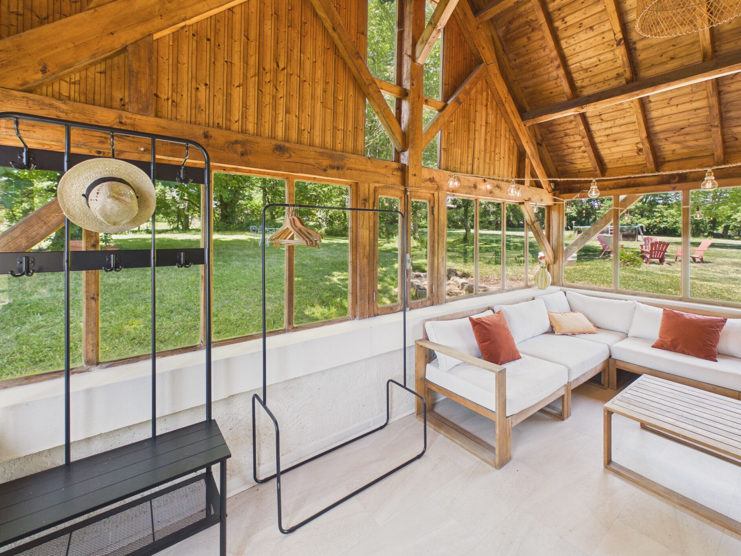 Interior de madera con un sofá blanco, un perchero colgante y vistas al exterior.