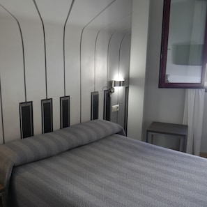 Una habitación de hotel moderna con una cama grande, una mesita de noche, una lámpara de pared y una ventana con cortinas.
