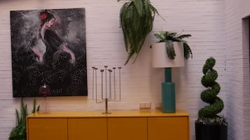 A yellow cabinet with a painting, a hanging plant, a lamp, and a spiral plant.