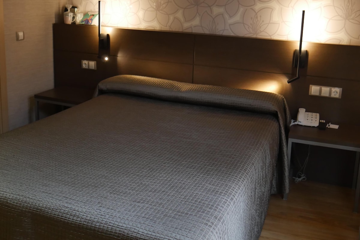 Quarto com cama, mesas de cabeceira, abajur e telefone.
