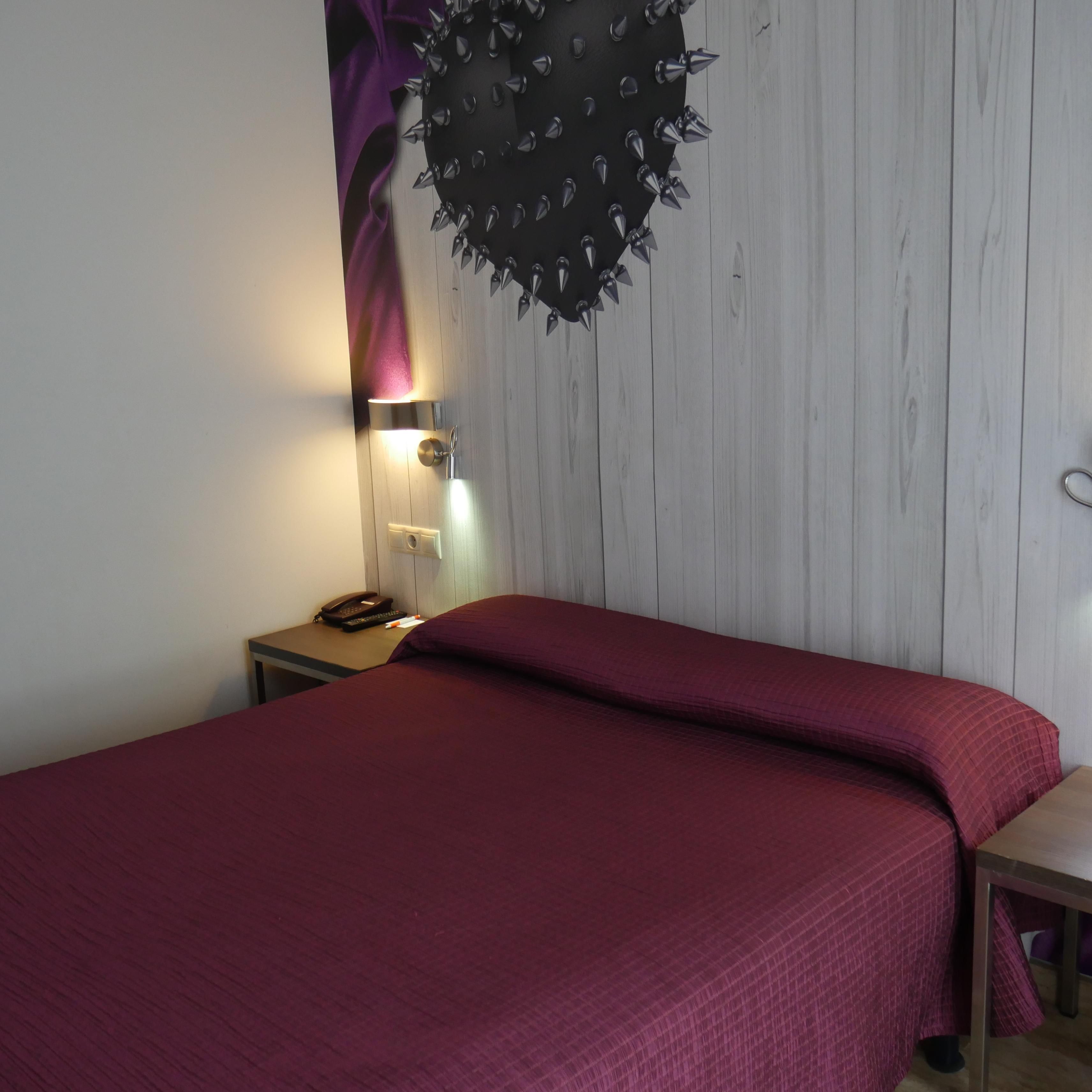 Quarto com cama, mesa de cabeceira, abajur e um enfeite na parede.