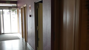 Un pasillo con puertas, un cartel de salida de emergencia y un letrero que indica la prohibición de fumar en caso de incendio.