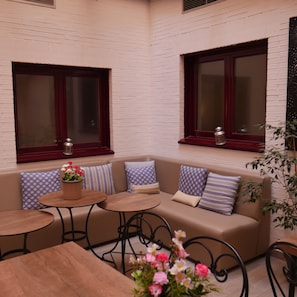 A cozy outdoor seating area with a cushioned bench, round tables, and potted plants. - 4C Cuatro Caminos (Madrid)