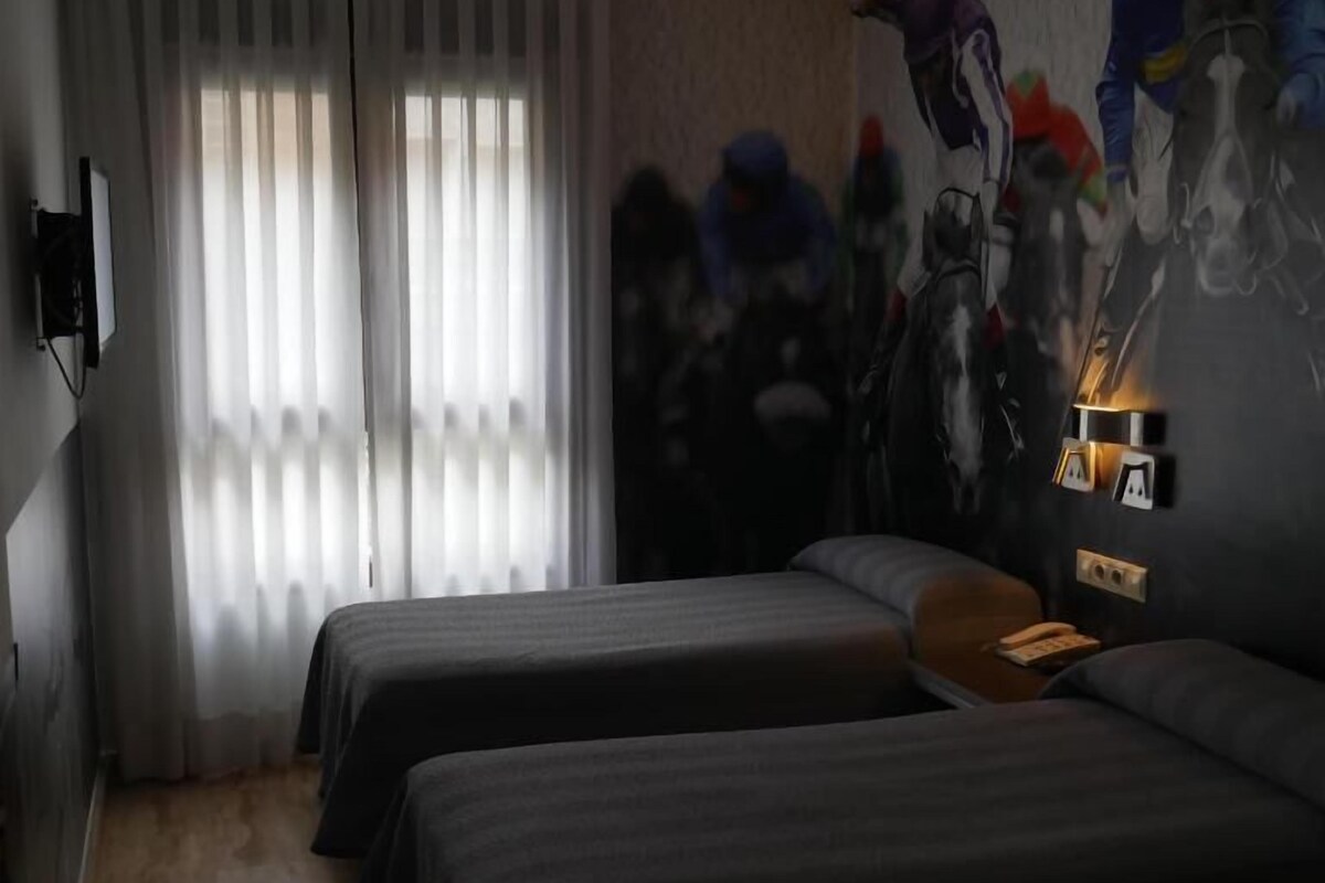Una camera d'albergo con due letti, un'ampia finestra con tende leggere, una TV a parete e un murale raffigurante fantini.