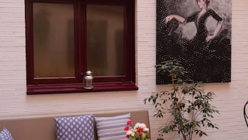 A room with a sofa, a window with a lantern, a painting, and a potted plant.
